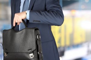 businessman holding leather briefcase checking time on his watch at the airport.
