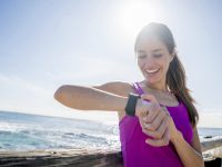 Young woman running outdoors by the beach using a smart watch to check her pulse and calorie countdown
